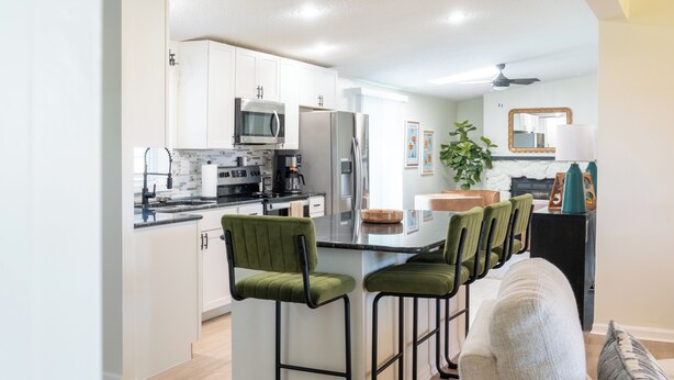 A modern kitchen with white cabinets, stainless steel appliances, and a central island with green bar stools. - Charming 3-bedroom Ranch Home in Grand Rapids - Perfect for Family Getaways! (Grand Rapids)