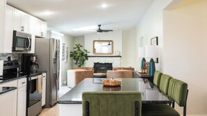 A modern kitchen with stainless steel appliances, a dining table with green upholstered chairs, and a fireplace. - Charming 3-bedroom Ranch Home in Grand Rapids - Perfect for Family Getaways! (Grand Rapids)
