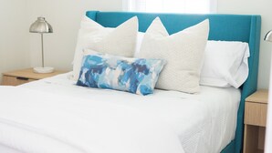 A bed with a teal headboard, white bedding, and a blue abstract pillow. - Charming 3-bedroom Ranch Home in Grand Rapids - Perfect for Family Getaways! (Grand Rapids)