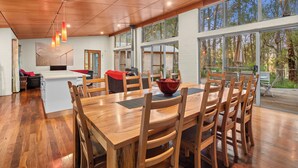 Un comedor amplio con una gran mesa de madera y sillas, una isla central con un tazón rojo y ventanas grandes que ofrecen vistas al exterior.