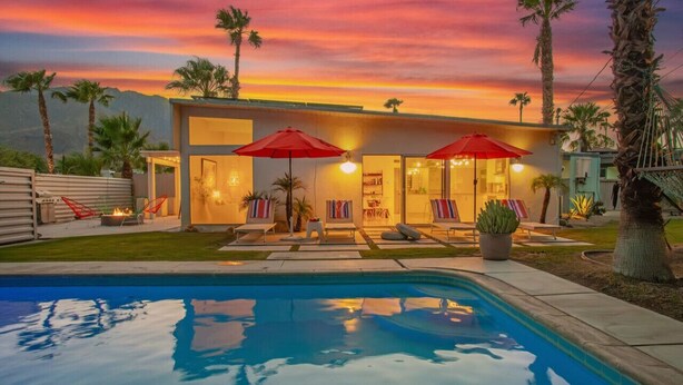 A modern house with a pool, red umbrellas, and palm trees at sunset. - Lush, secluded desert oasis w/pool & EV charger (Palm Springs)