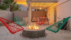 A patio with a fire pit, outdoor seating, and a pergola with string lights. - Lush, secluded desert oasis w/pool & EV charger (Palm Springs)