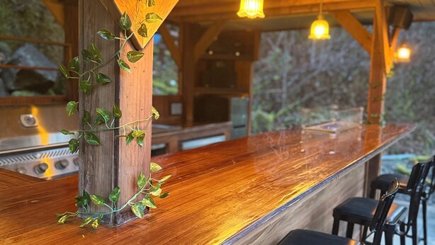 A wooden bar with hanging lights, a grill, and bar stools. - Private Romantic Woodland Getaway- sauna, hot tub, outdoor culinary bar, gardens (Vader)