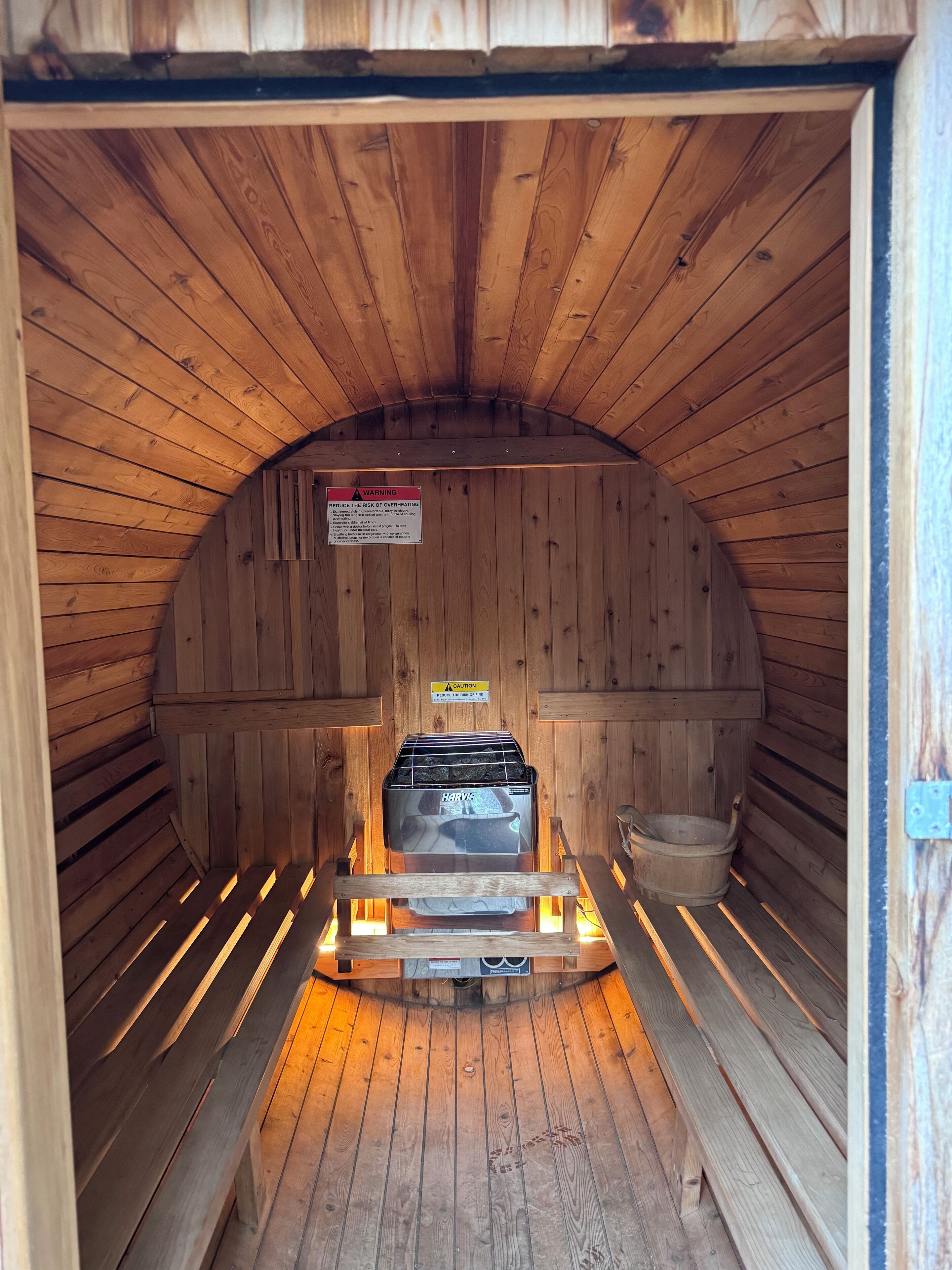 Een sauna met houten wanden en een bankje. Er is een waarschuwingsteken om het risico op oververhitting te verminderen.