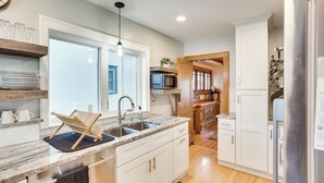Una cocina moderna con armarios blancos, encimera de granito, microondas integrado y refrigerador de acero inoxidable.