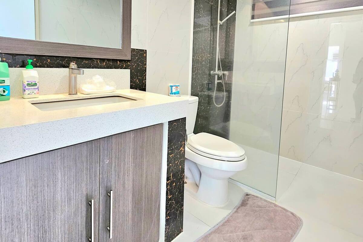 A modern bathroom with a marble vanity, a toilet, and a glass-enclosed shower.