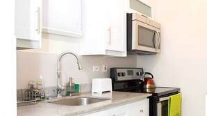 Une cuisine compacte avec des meubles blancs, une cuisinière en acier inoxydable, un four à micro-ondes et une bouilloire.