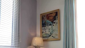 Un salon avec un canapé, une lampe, un tableau et une fenêtre avec des stores.