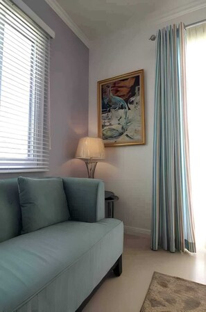 Een woonkamer met een bank, een lamp, een schilderij en een raam met jaloezieën.