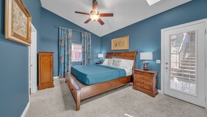 A bedroom with a bed, nightstands, a ceiling fan, a door with a view, and a window with curtains.