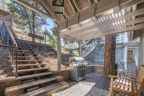 A covered outdoor area with a grill, wooden steps, and a bench. - Evergreen Chalet with hot tub in Big Bear (Big Bear city)