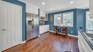 A kitchen with white cabinets, a stainless steel refrigerator, and a dining table with chairs.