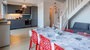 Une cuisine moderne avec des meubles gris, un coin repas agrémenté d’une nappe à motifs et un escalier avec des rampes blanches.