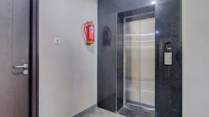 Un ascenseur avec une finition métallique, un extincteur fixé au mur et une porte dotée d’une poignée.