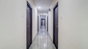 Un long couloir étroit, avec des portes en bois sombre de chaque côté et un sol brillant, parsemé de motifs.