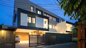 A modern two-story house with a garage, a gated driveway, and a number sign indicating the property number. - Ekkamai Villa Sleeps 12 with Cinema (Bangkok)
