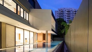 A modern building with a swimming pool, glass walls, and a dining area. - Ekkamai Villa Sleeps 12 with Cinema (Bangkok)