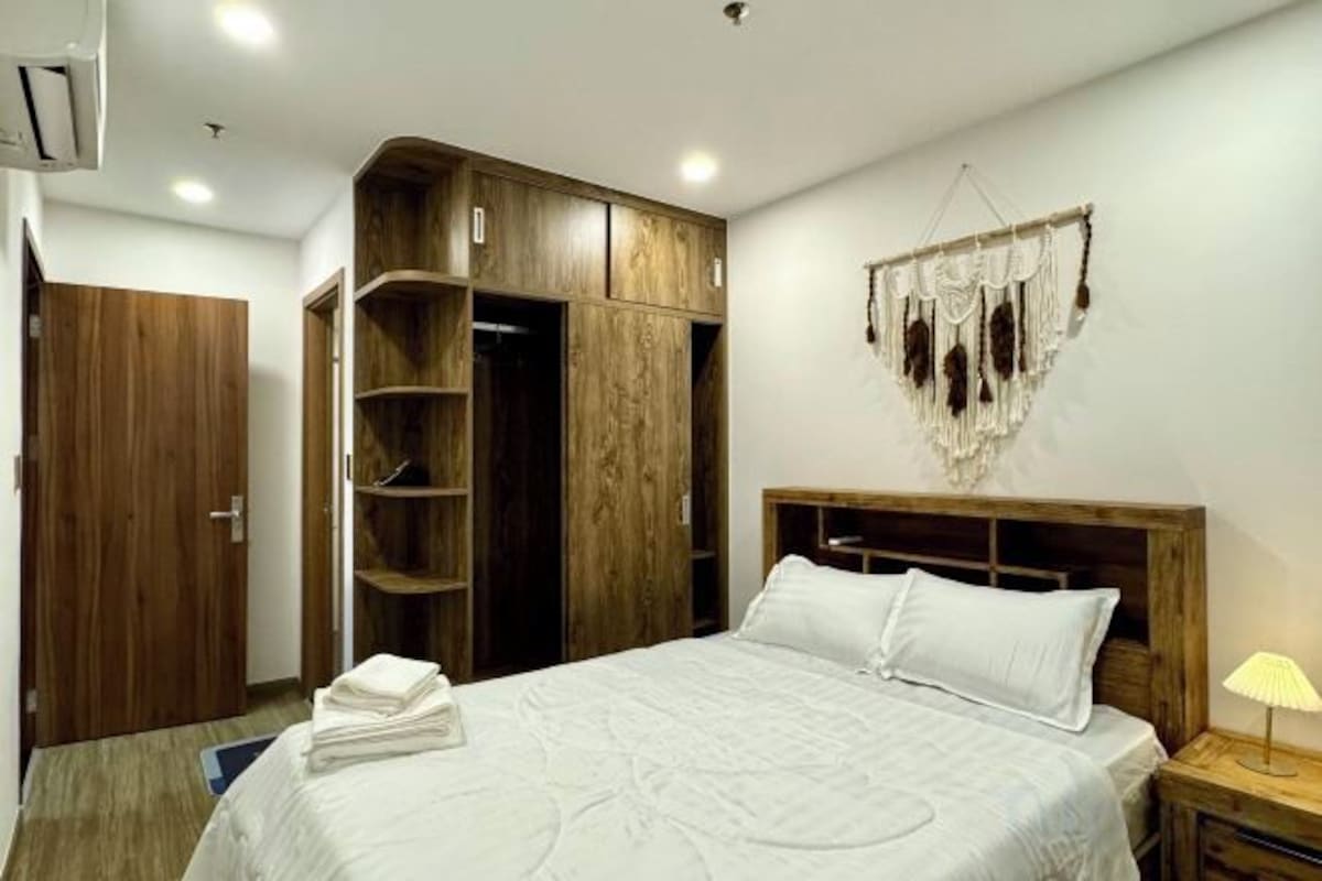 A bedroom with a bed, wooden wardrobe, and a wall-mounted hanging decoration.