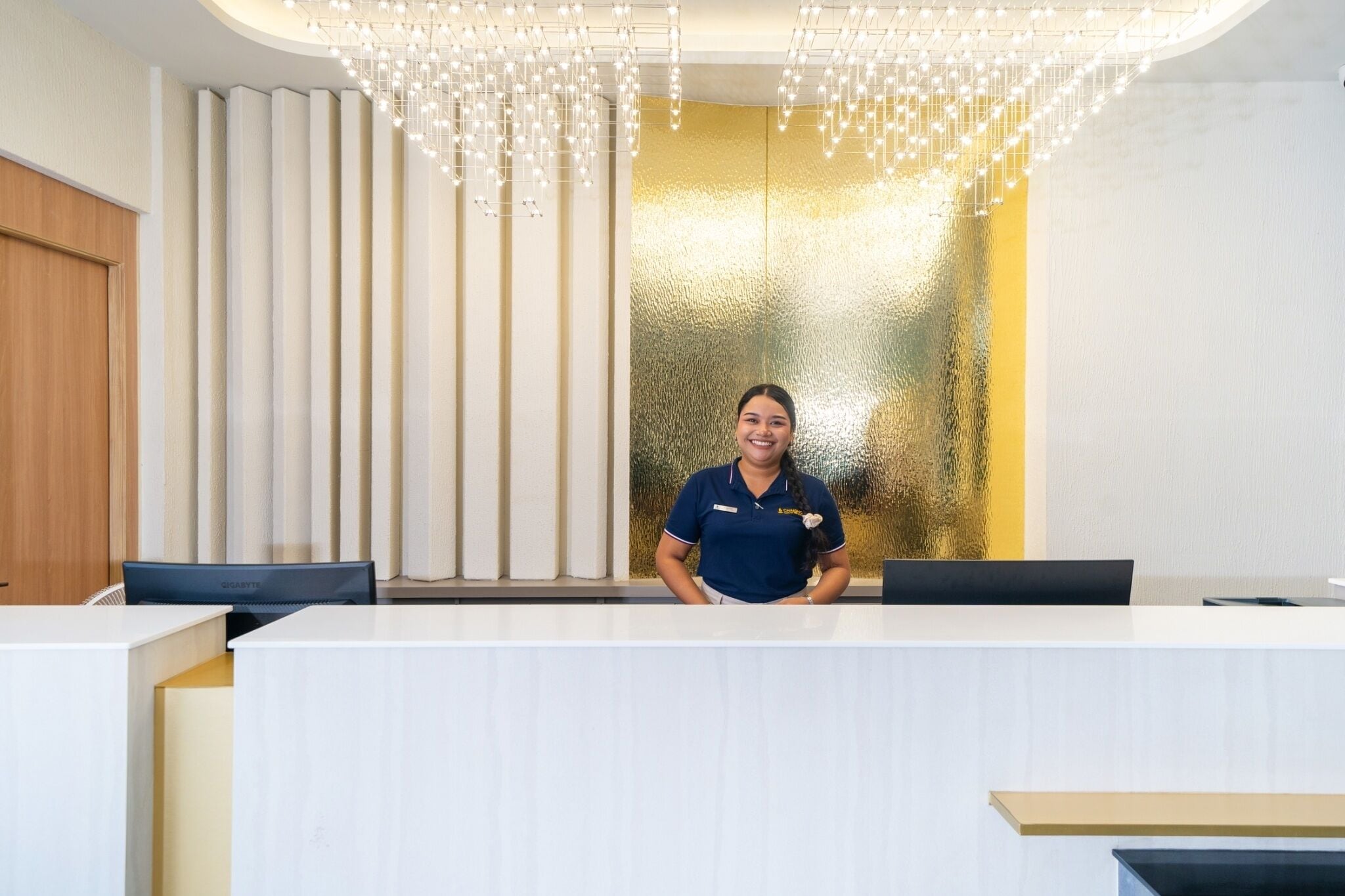 A reception desk with a modern design, featuring a white counter and a decorative light fixture above.