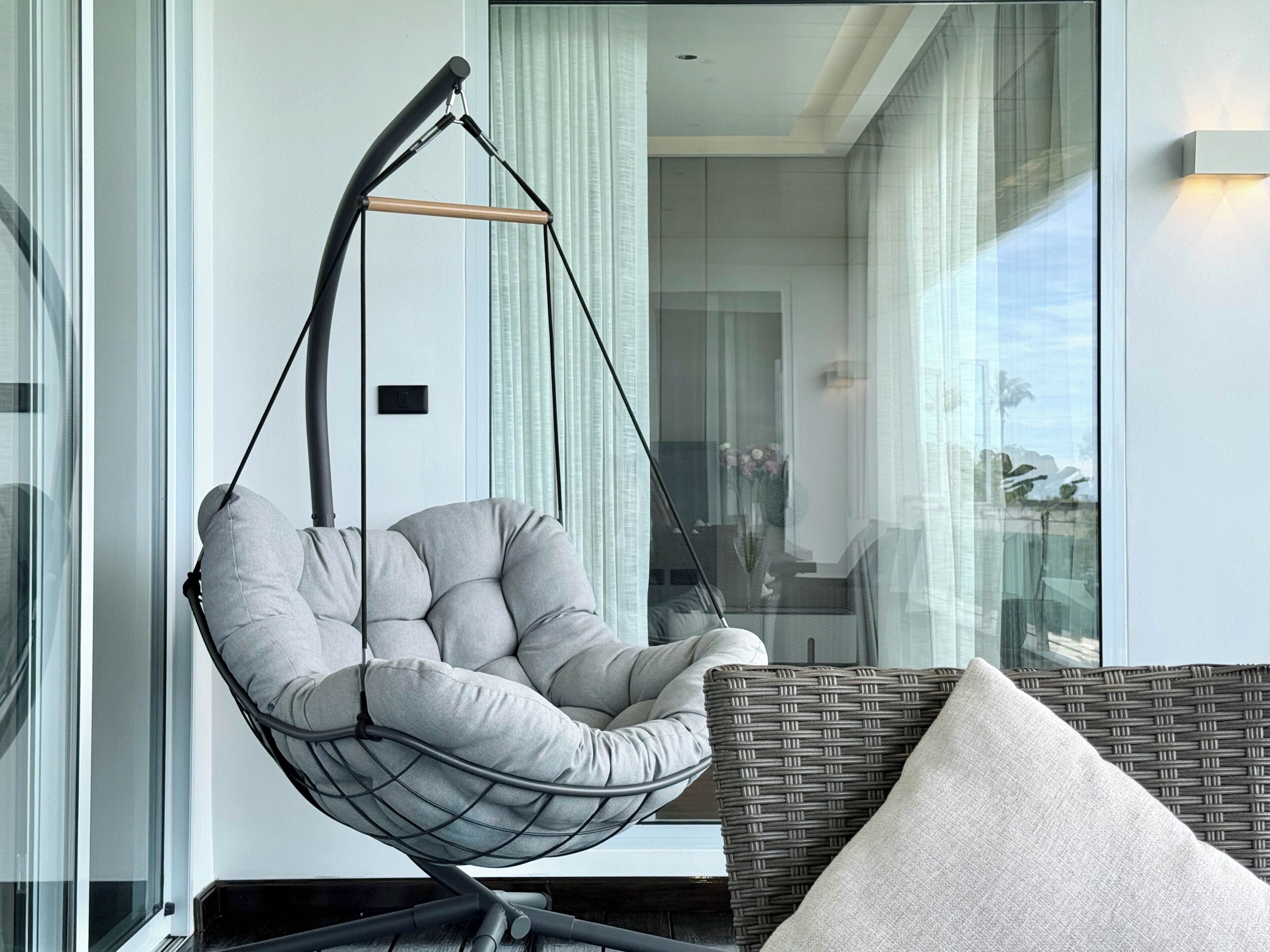 A modern room with a hanging chair, a wicker sofa, and a view through large windows.