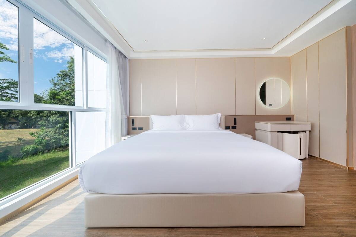 Ein modernes Schlafzimmer mit einem großen Bett, einem Nachttisch, einem Spiegel und Blick auf Grünfläche.