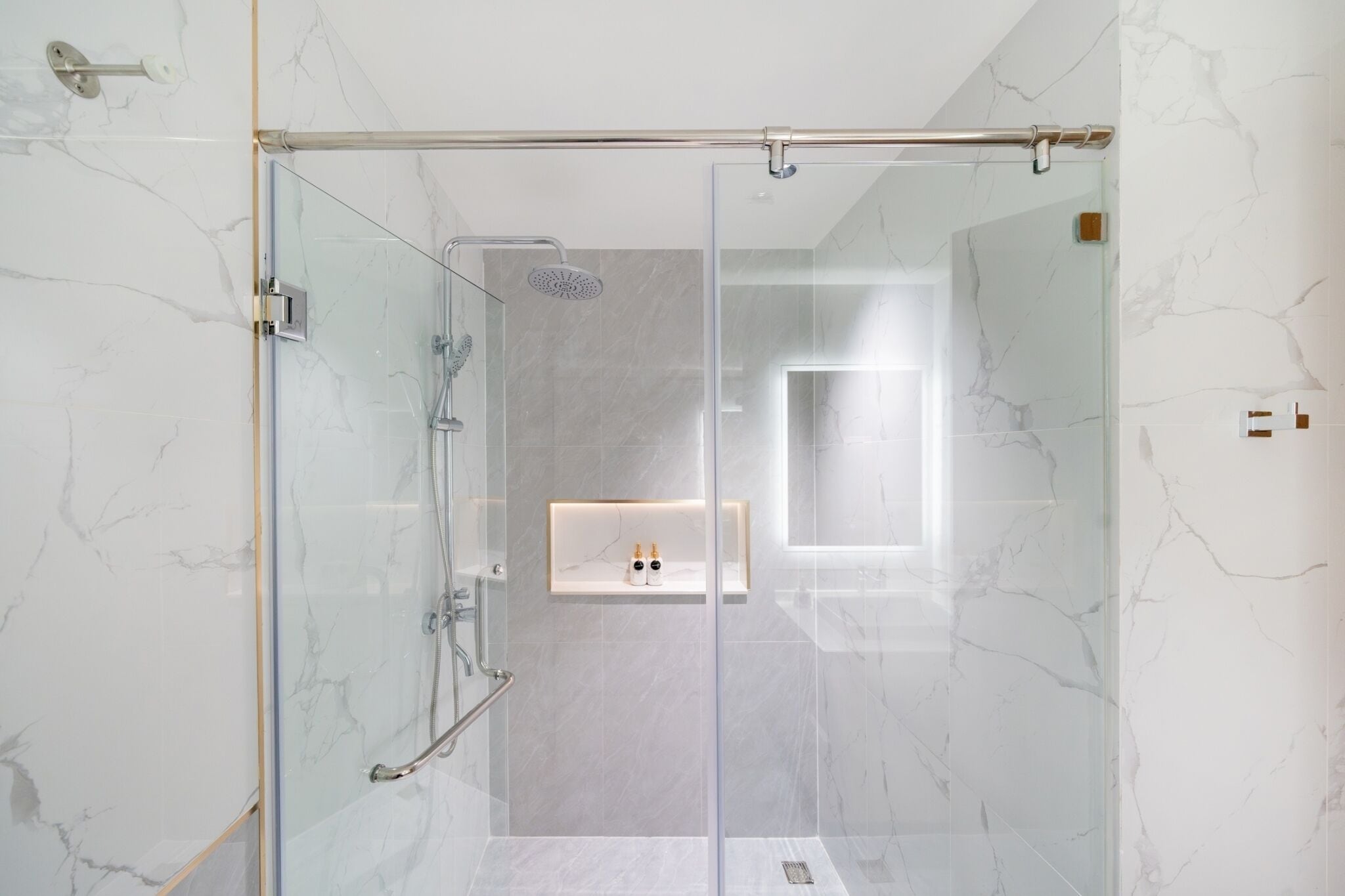 A modern bathroom with a glass-enclosed shower, marble walls, and a built-in sink with a mirror.