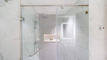 A modern bathroom with a glass-enclosed shower, marble walls, and a built-in sink with a mirror.