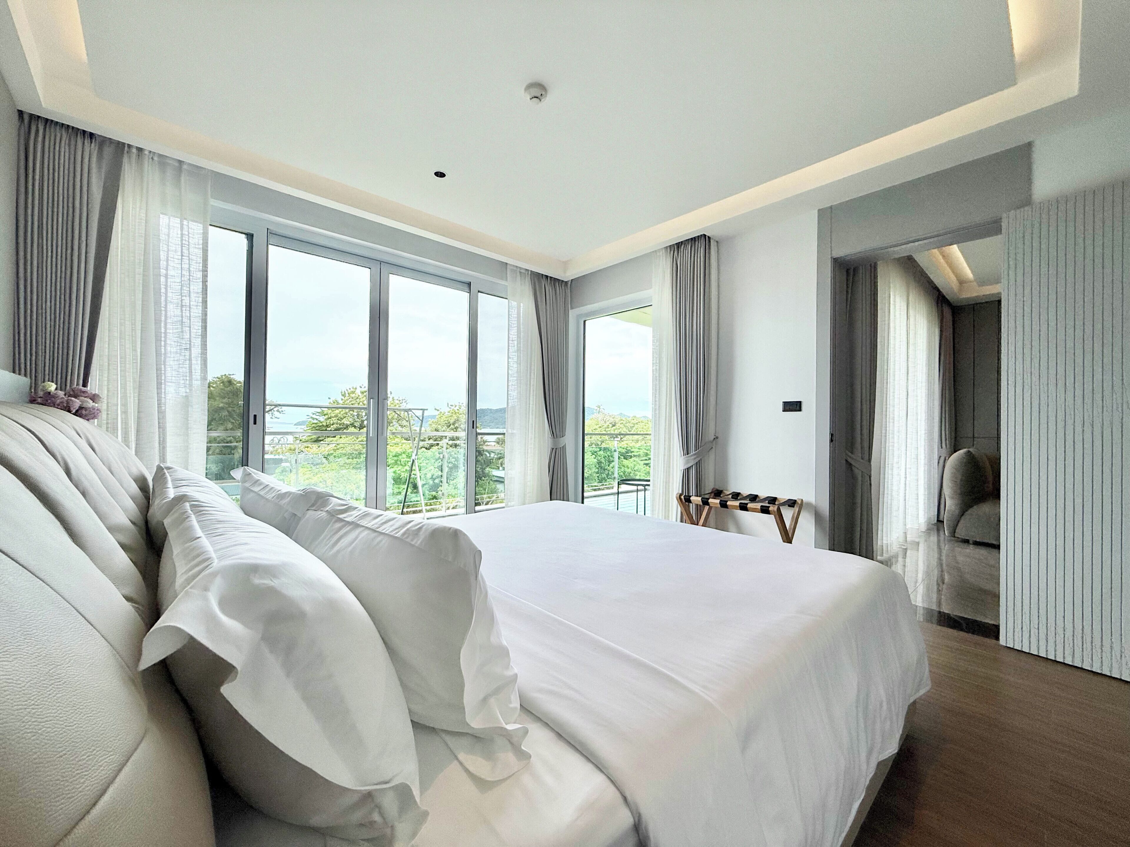 A modern bedroom with a large bed, a view of greenery, and a balcony.