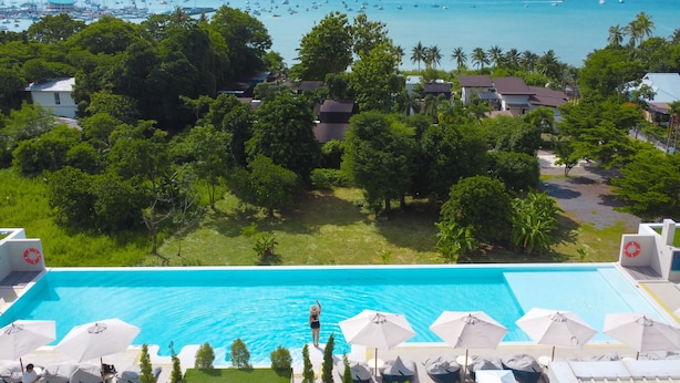 A swimming pool with lounge chairs and umbrellas, surrounded by lush greenery and a view of boats on the water. - Chalong Marina Bay View Phuket (Rawai)