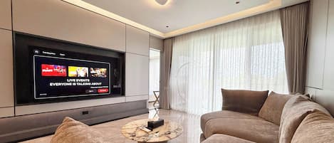 A modern living room with a large flat-screen TV, a marble coffee table, and plush sofas.