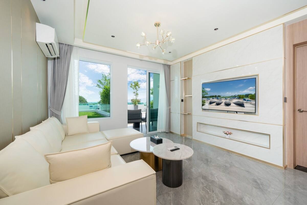 Ein modernes Wohnzimmer mit einer Couch, einem runden Couchtisch, einem an der Wand montierten Fernseher und Blick ins Freie.