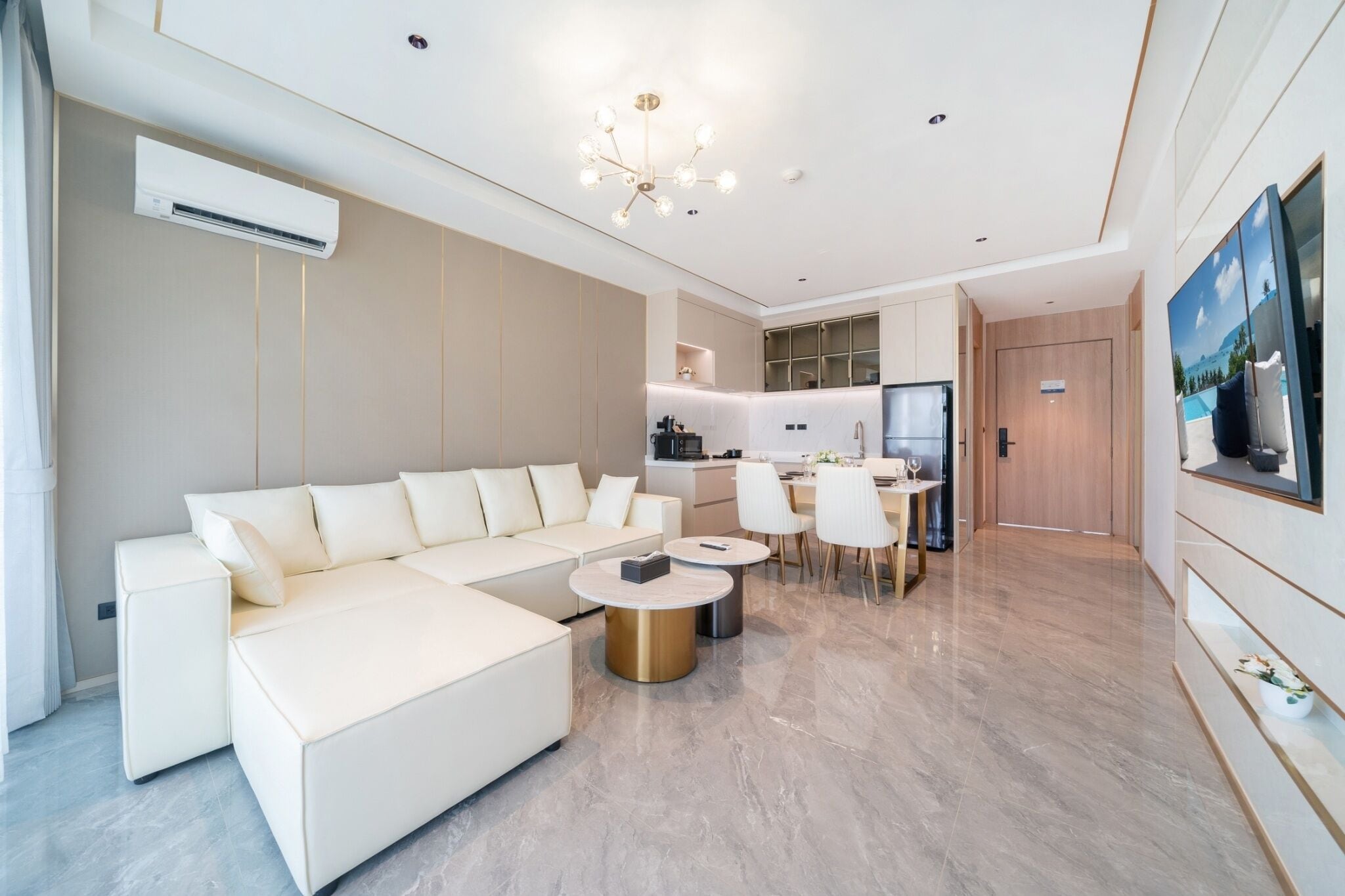 A modern living room with a white sectional sofa, a dining area with a table and chairs, a kitchen with a refrigerator, and a large painting on the wall.