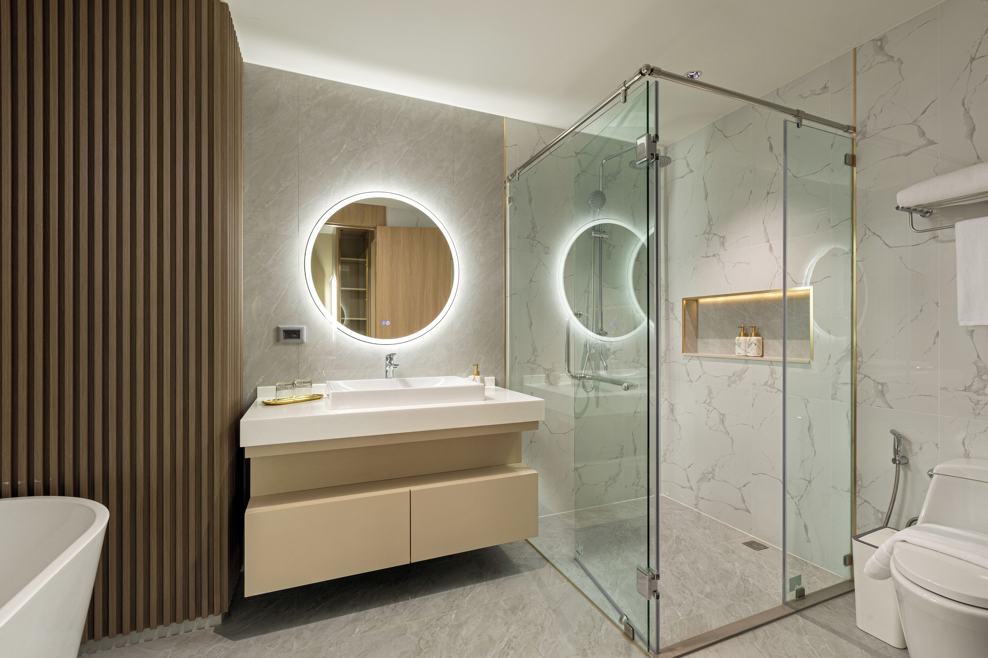 A modern bathroom with a glass-enclosed shower, a round mirror with a light, and a beige vanity.