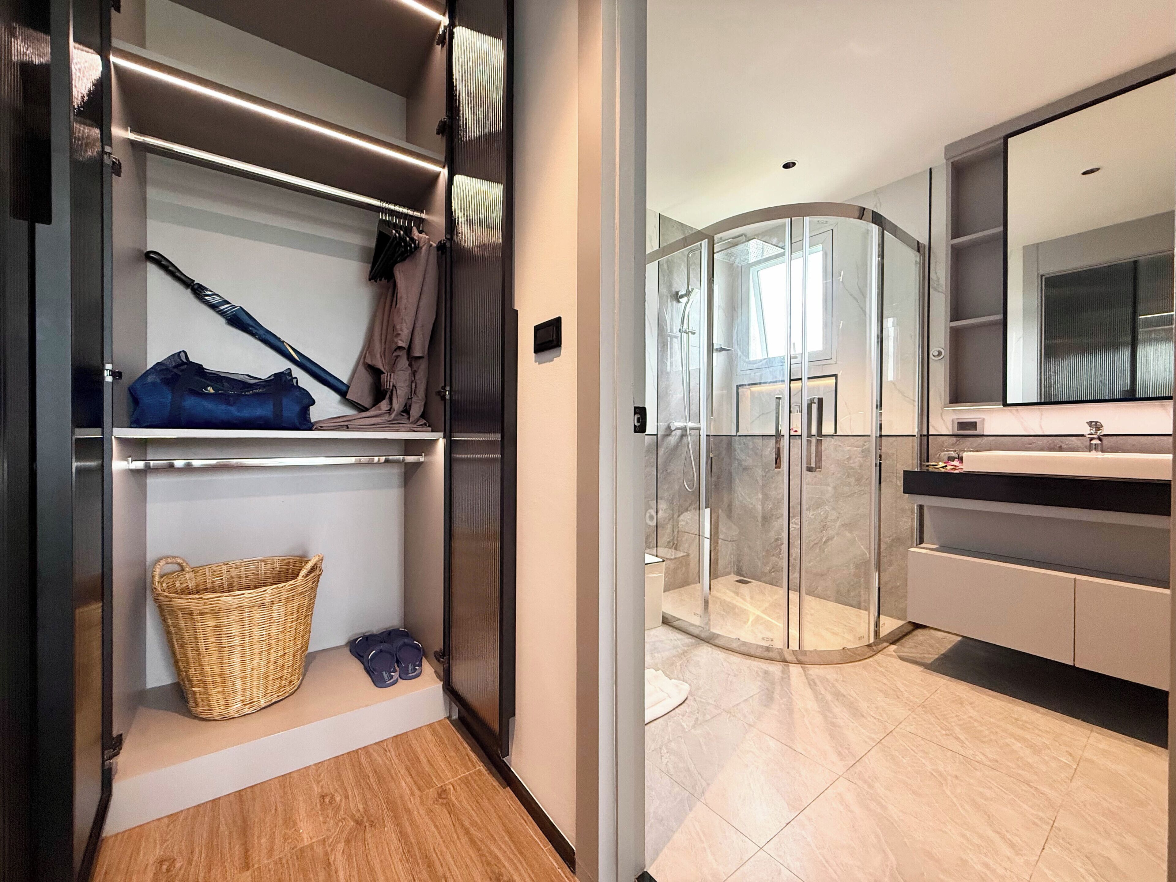 A modern bathroom with a glass shower enclosure, a large mirror, and a wooden floor.