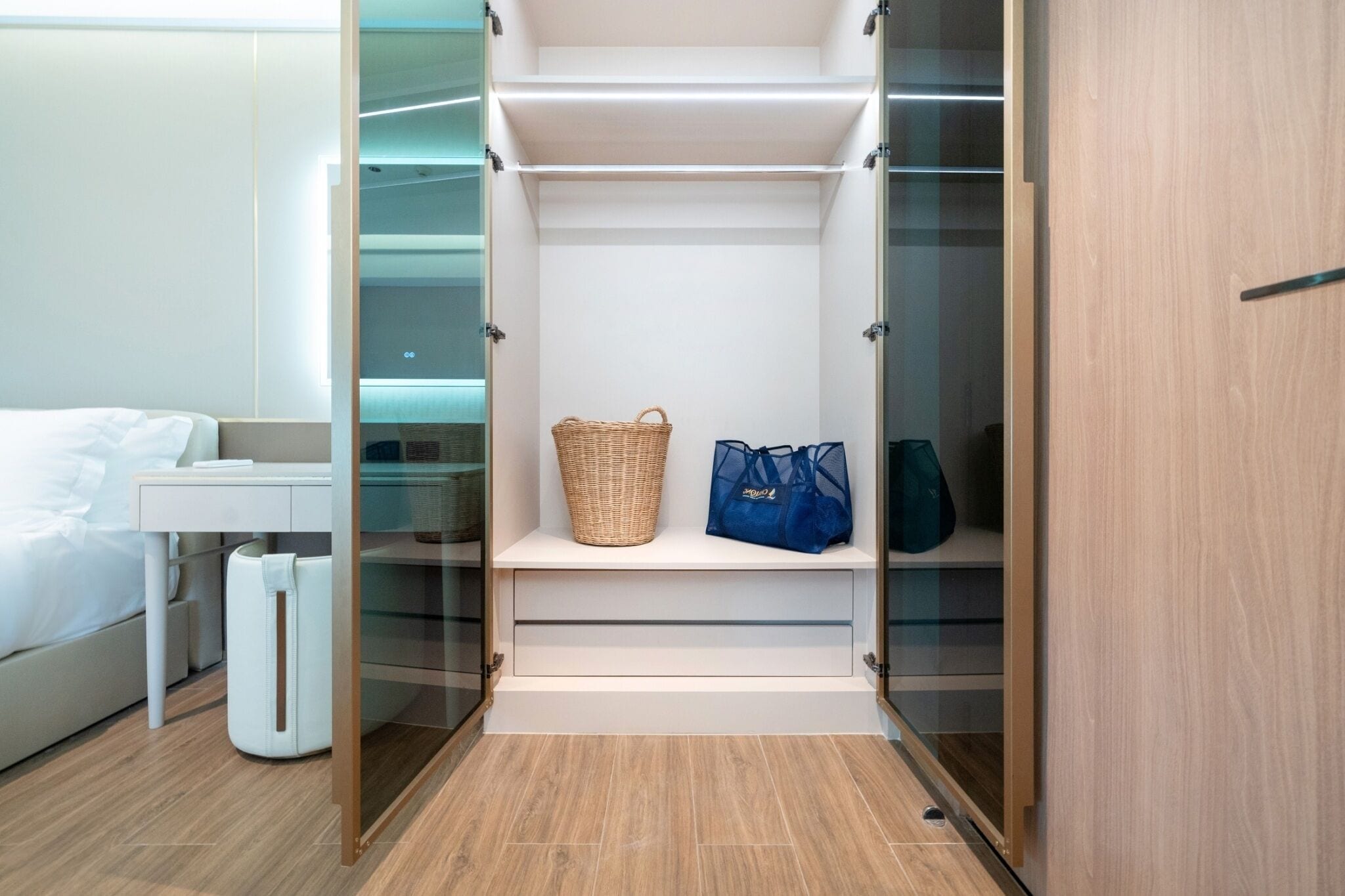 A hotel room with a bed, a bedside table, a white trash bin, and a built-in closet with shelves and a basket.