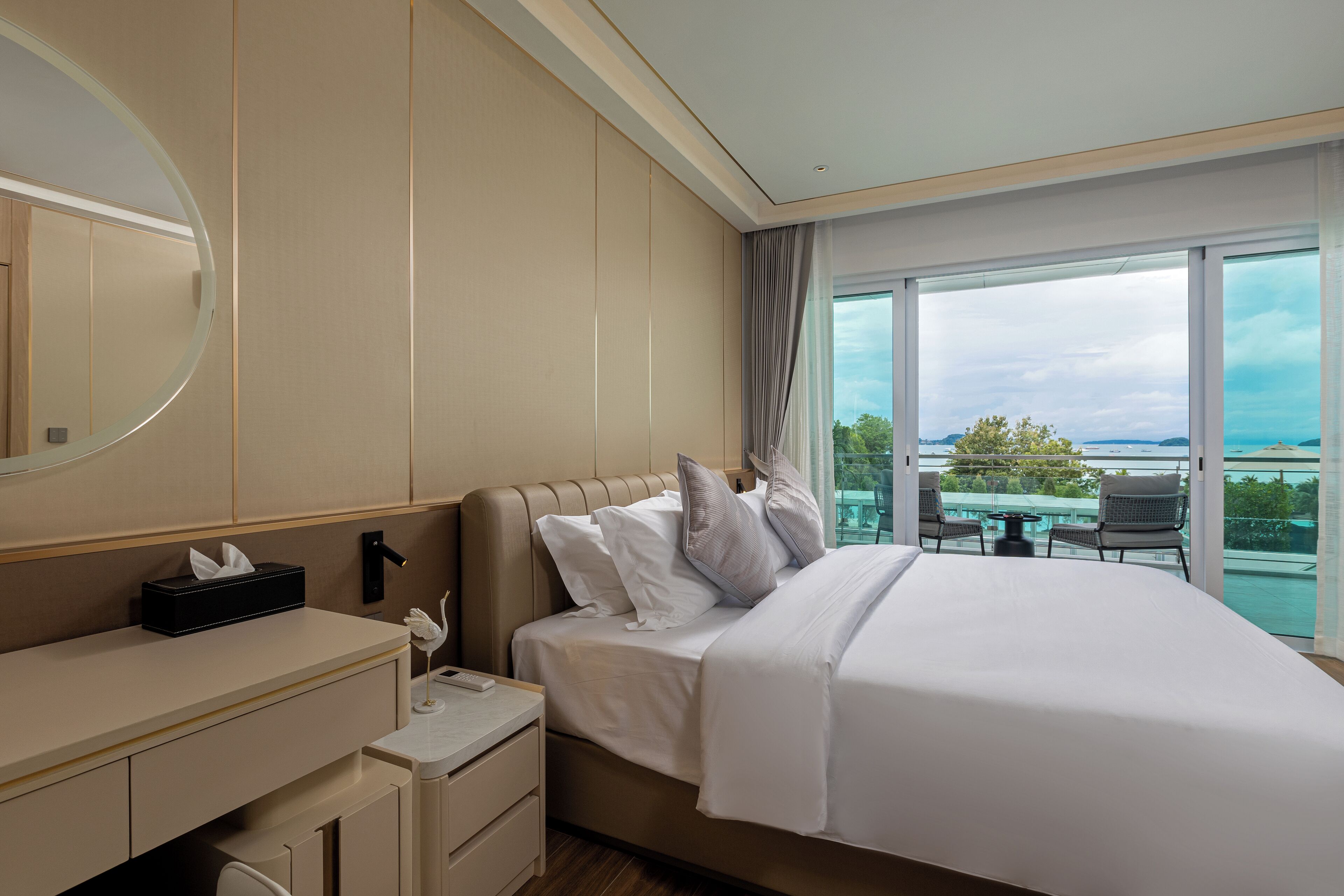 A hotel room with a bed, bedside table, and a large window offering a view of the outdoors.