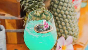 A bar setting with a glass of blue cocktail, a pineapple, and a keyboard on the counter.