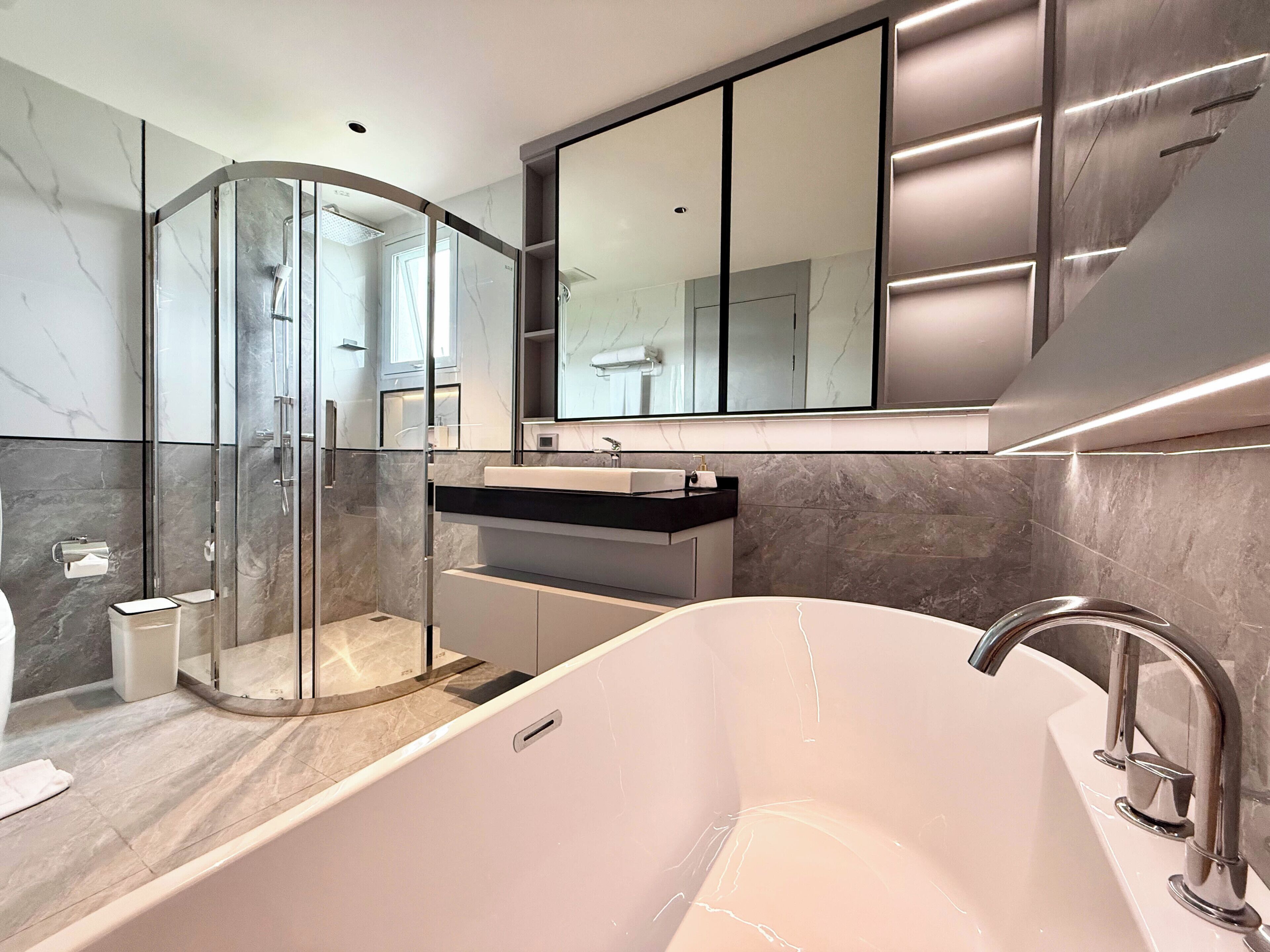 A modern bathroom with a glass-enclosed shower, a freestanding bathtub, and a large mirror above the sink.