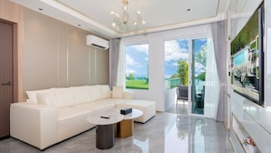 A modern living room with a sectional sofa, a round coffee table, and a large TV screen. - Chalong Marina Bay View Phuket (Rawai)