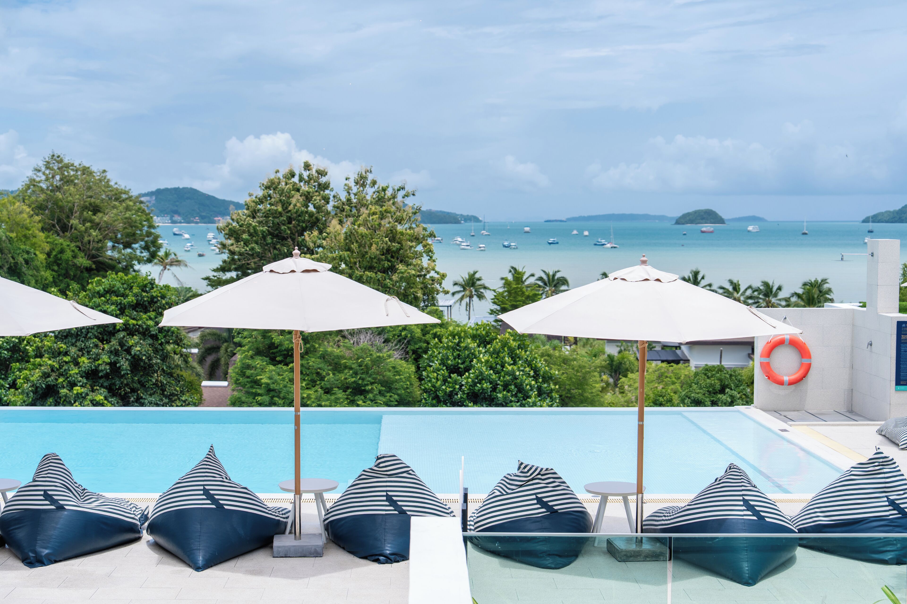 A poolside area with lounge chairs and umbrellas, overlooking a body of water with boats.