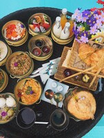 A tray with various dishes, including rice, soup, and bread, along with condiments and a bouquet of flowers.