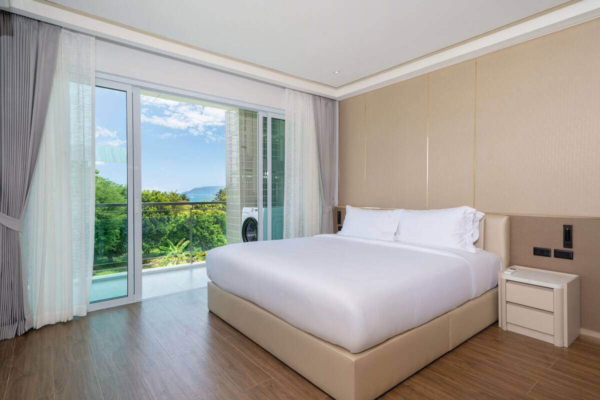 Ein modernes Hotelzimmer mit einem großen Bett, einem Nachttisch und Blick auf Grün hinter einer Schiebetür.