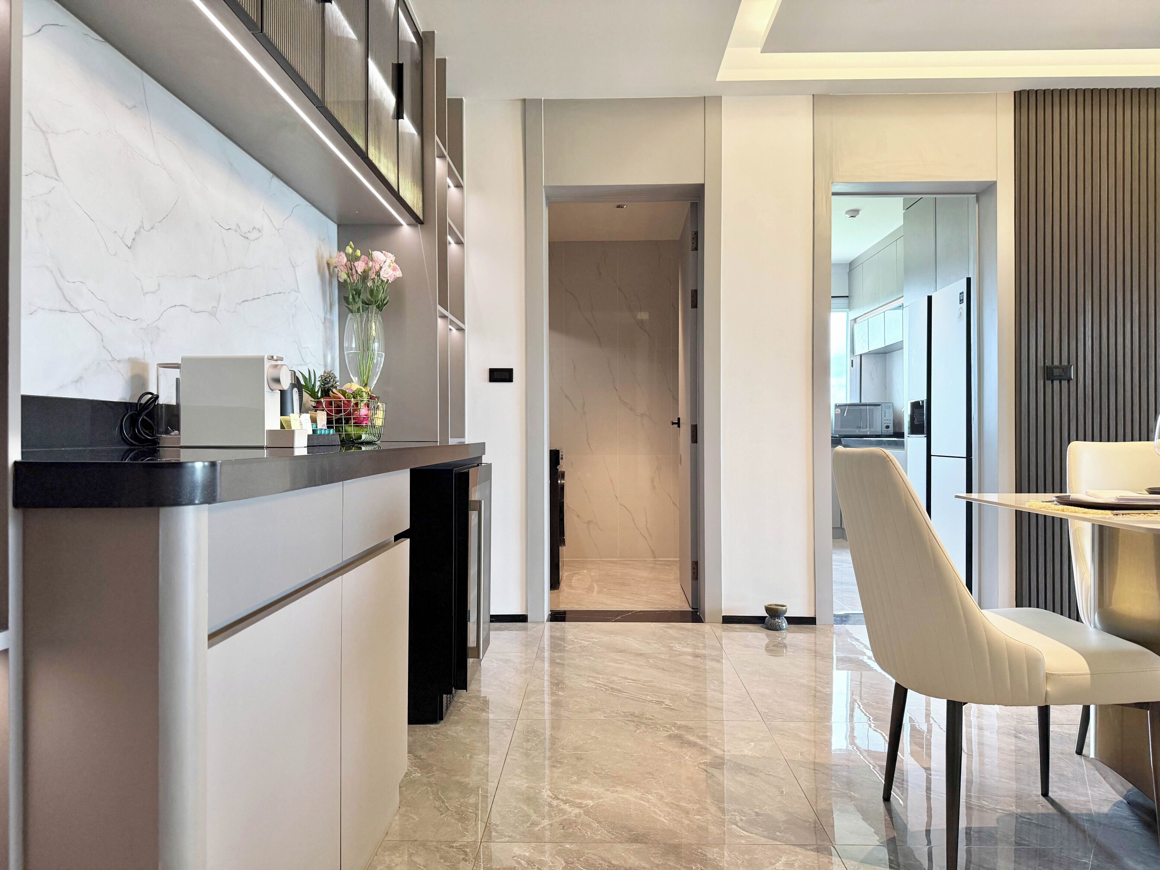 A modern kitchen with a marble backsplash, a dining area with a chair, and a hallway leading to another room.