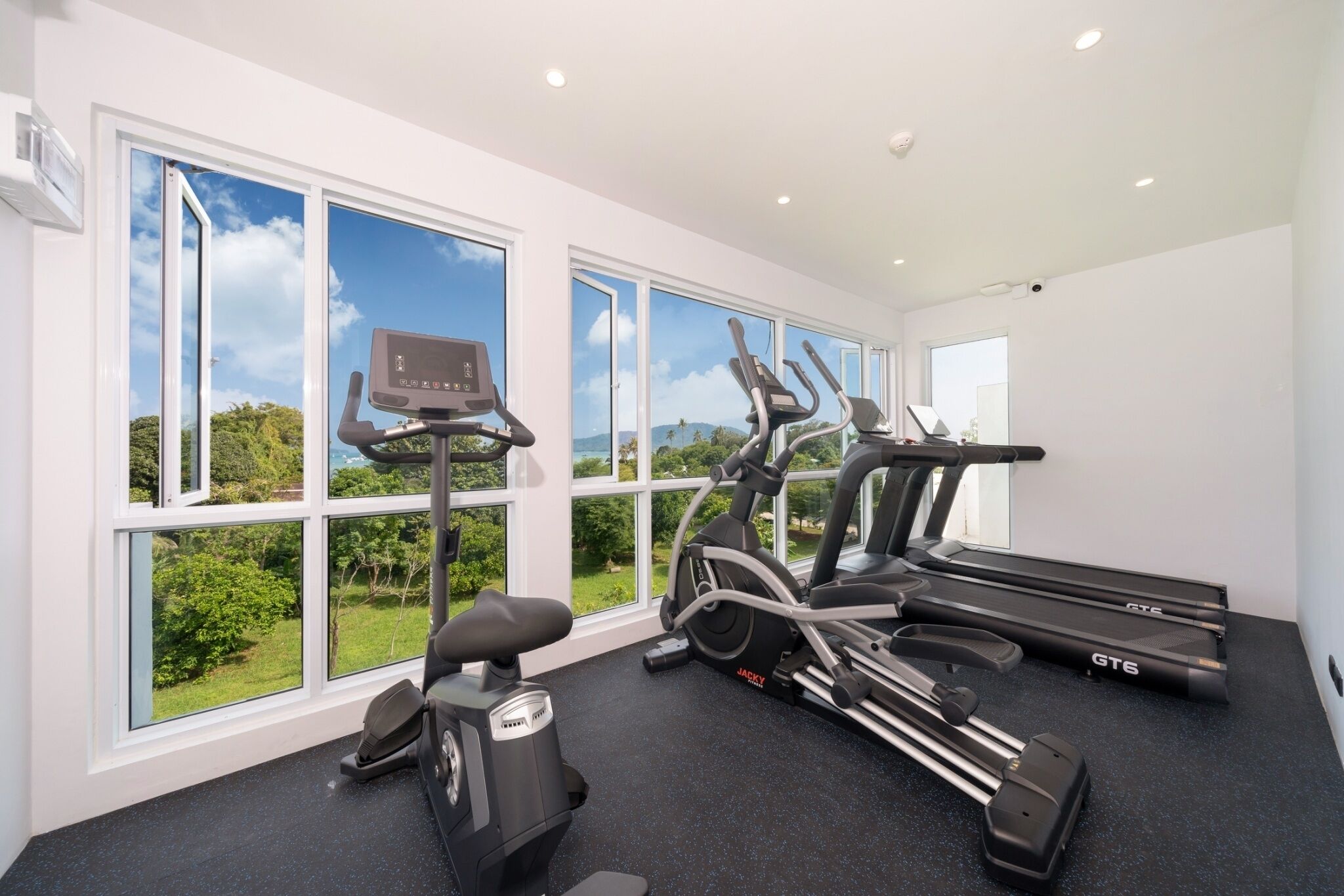 Un gimnasio con equipo de ejercicio, ventanas amplias y vistas al verdor.