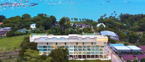Un hotel con varios pisos, una piscina y vistas al mar con barcos.