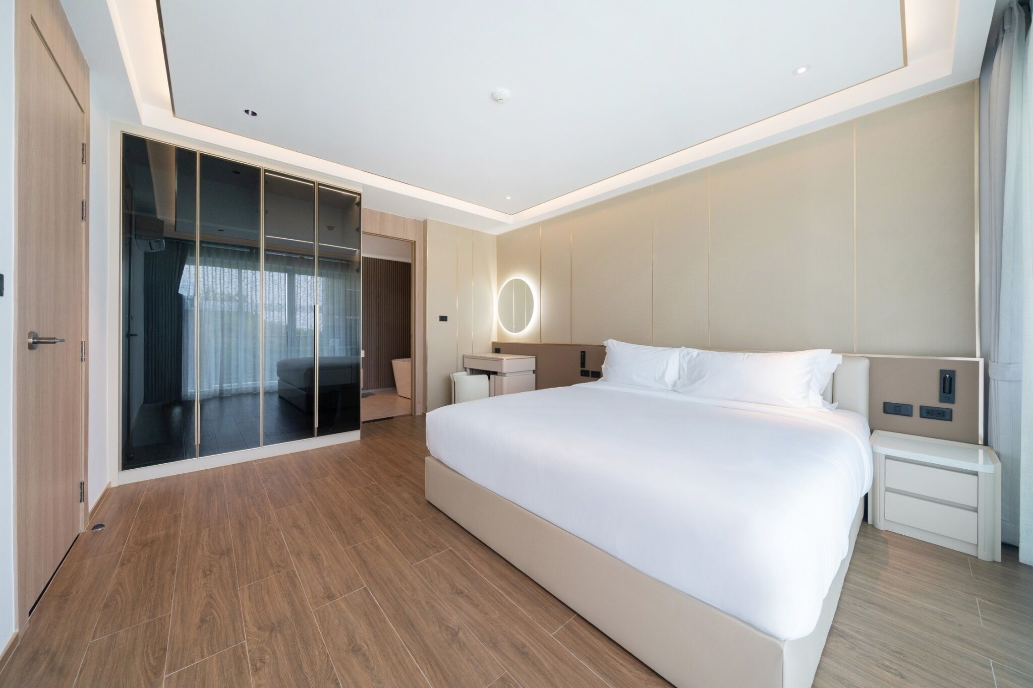 A modern hotel bedroom with a large bed, a walk-in closet, a bedside table, and a circular light fixture.