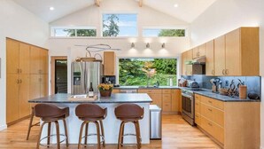 Une cuisine moderne dotée d’un grand îlot central, de meubles en bois et offrant une vue sur la verdure environnante.