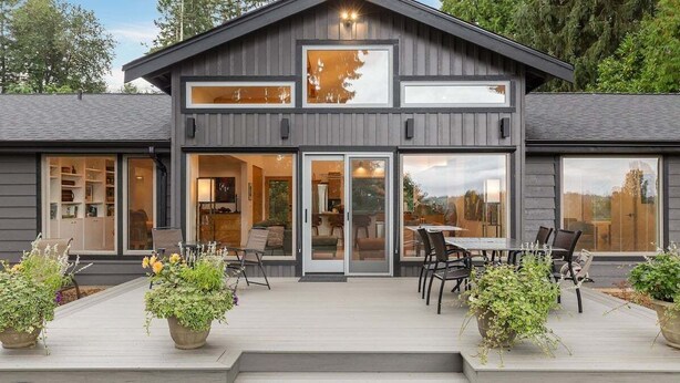 Une maison moderne à deux étages, dotée de grandes portes-fenêtres coulissantes, d’un patio avec mobilier d’extérieur et de plantes en pot.