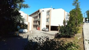 Un edificio moderno con techo plano, varios pisos y un estacionamiento al frente.