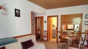 Una sala de estar con un sofá a rayas, una mesa de comedor con sillas y una cocina visible a través de un umbral abierto.